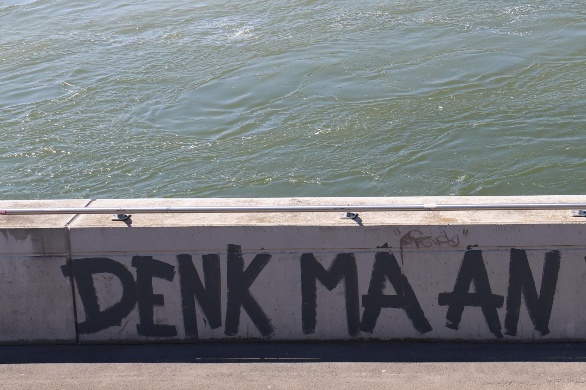 Graffiti an Flussbrüstung mit der Aufschrift Denk ma an