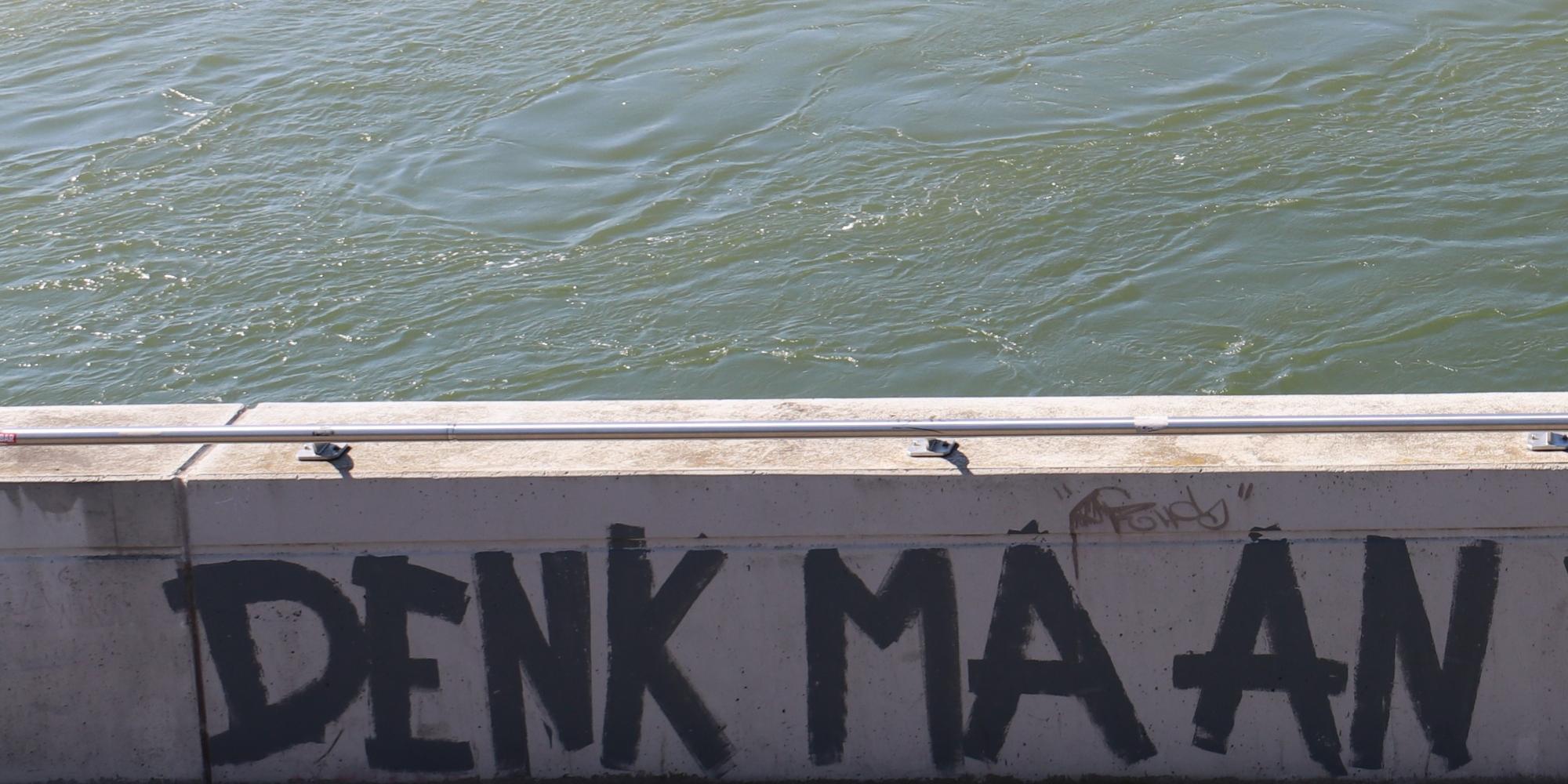 Graffiti an Flussbrüstung mit der Aufschrift Denk ma an